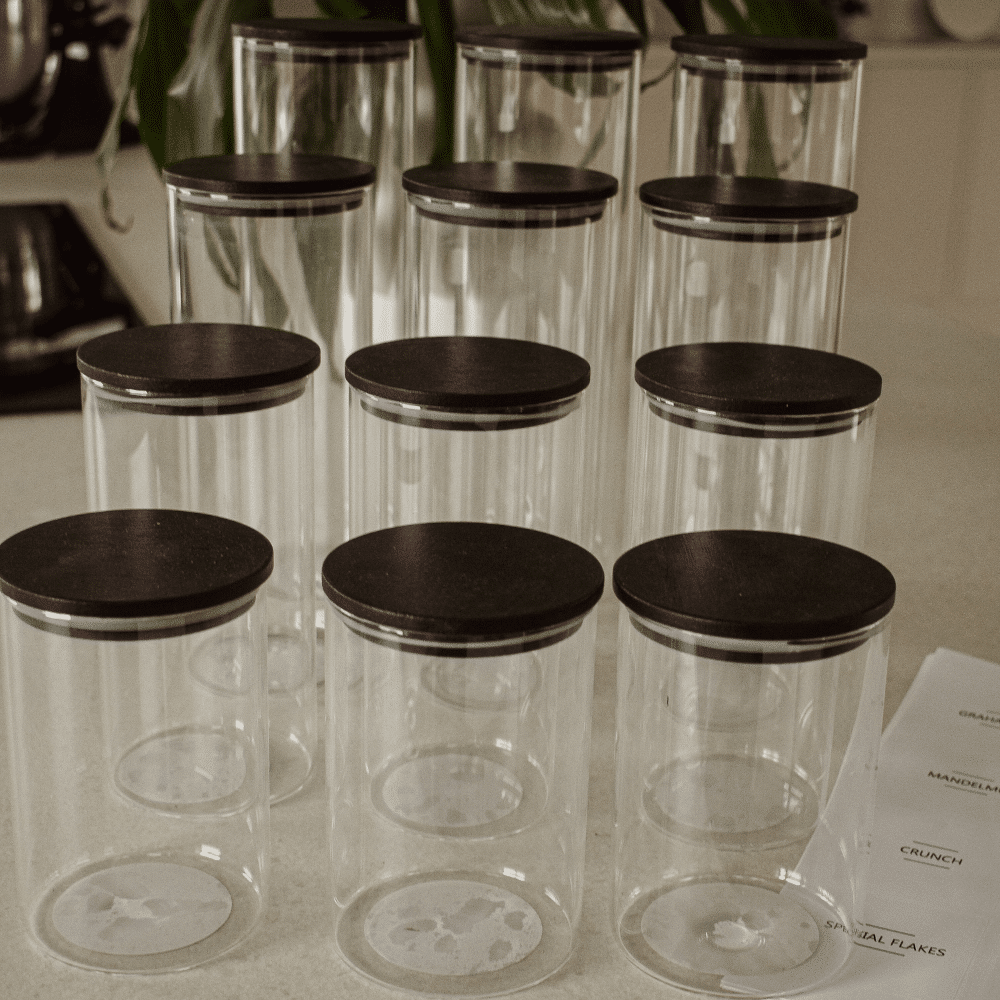 opbevaringsglas med sort bambus låg | Runde opbevaringsglas med sort bambuslåg fyldt med mel, havregryn og pasta – stående på hylde i køkken.