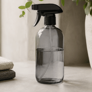 Grå sprayflaske i glas med sort sprayhoved på stilrent badeværelse med grøn plante.